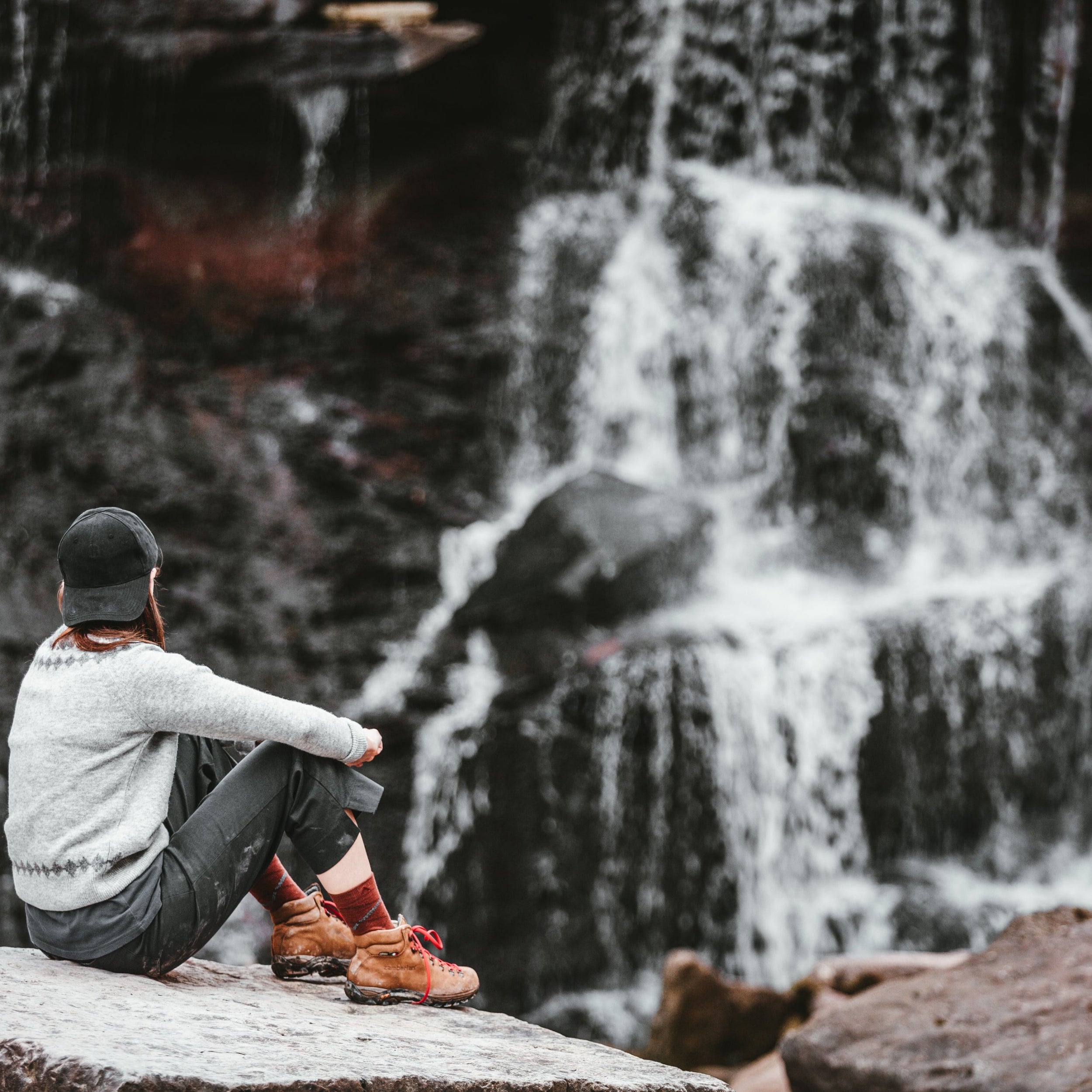 Person sitting on a rock in front of a waterfall